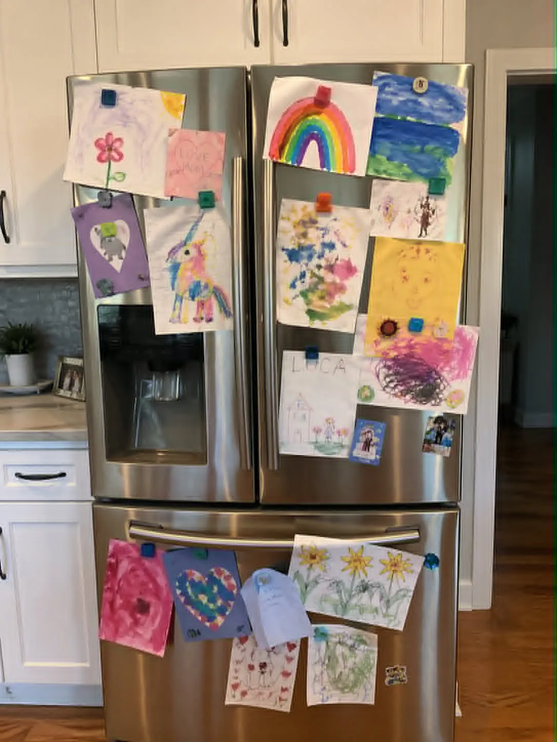 Refrigerator covered in layers of children's artwork held up by magnets